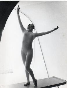 Cecilia Baram dancing on a bench, wearing a long-sleeved leotard with her arms lifted in the air