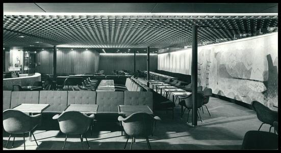 A room with a low, textured ceiling, full of tables, chairs, and booths