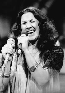 Flora Purim singing on a stage, holding a microphone in each hand