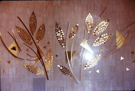 An abstract metal sculpture of gold-colored branches and leaves made out of triangles, mounted on a wooden wall