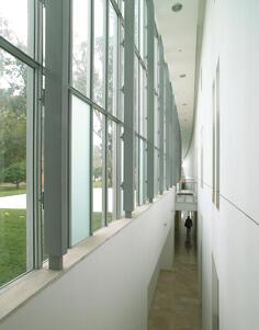 A white-paneled hallway with high ceilings and a wall of tall windows