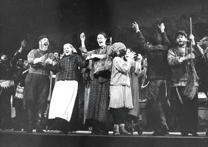 Bea Arthur as Yente in Fiddler on the Roof - center of a row of people singing in musical