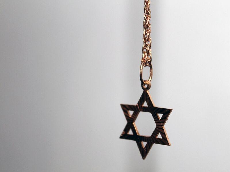 Gold Star of David necklace hanging in midair, in partial focus.