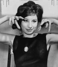 Barbra Streisand in black dress, hands up near face, half-length portrait, facing front