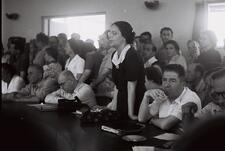 A large group of people in a crowded room. Beba Idelson stands behind a curved desk, speaking.
