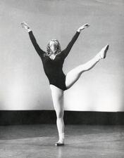 Cecilia Baram dancing, one leg lifted above her waist, both arms raised and her face tilted up