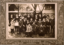 A group of children sitting and standing with a teacher standing behind them