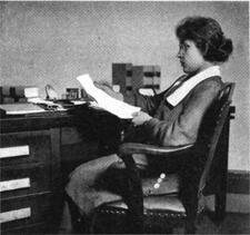 Anna Moscowitz Kross sitting at a desk, not looking at the camera, reading some papers.