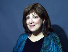 Portrait of Avivah Zornberg looking into camera in front of a blue background photographed by Joan Roth