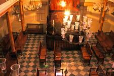 High-angle view of a room with a natural wooden Torah ark and benches, chandeliers, and checkered floor tiles