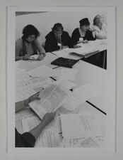 A group of women sitting at some tables pushed together, reading packets of paper
