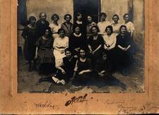 A group of women and girls, standing and seated, outside a building