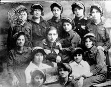 A group of thirteen young women in work clothes and caps