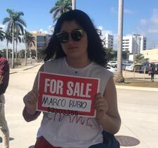 Lila Goldstein holding a sign that reads "For Sale: Marco Rubio"