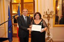 Karen Sarhon in a black dress receiving the Chevalier des Arts et des Lettres from the French Ministry of Culture in a formal state room