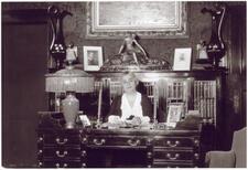 Lillian Freiman seated behind her desk and surrounded by small sculptures, candlesticks, ornate lamps, and framed photographs. 