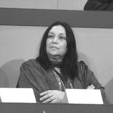 Naomi Shemer sitting at a panel table, arms crossed, listening to someone off-camera