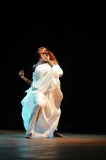 Minalu Degia dancing on stage, wearing a voluminous dress of crimped white cloth