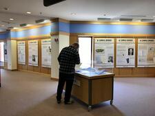 Person leaving over an exhibition display box in center of room with exhibition posters and signage on walls in background