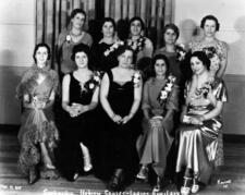 5 women seated in the front row and 5 women standing in the back row, smiling and wearing formal dresses