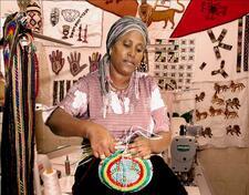 A woman weaving, sitting in a tent with other woven objects and patterns hung around her