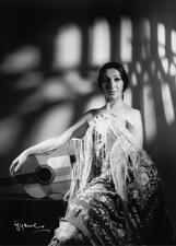 A studio portrait of Silvia Doron, wrapped in a fringed blanket, posing next to a guitar