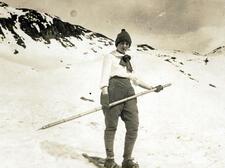 A young woman on a mountain, holding a single wooden ski pole
