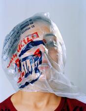 A portrait of Vered Nissim with a clear plastic shopping bag over her head. Printed writing on the bag covers half her face, the other half is unobstructed.