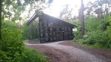 A metal and dark glass structure in the woods, with a slanting roof. The windows have white writing and black-and-white portraits etched on them.