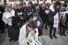 Women in prayer holding prayer books wearing tefillin and tallit