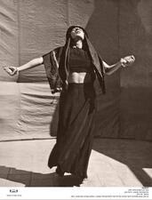 A woman wearing a black veil, black crop top, and long black skirt, her face tilted towards the sky and her arms out