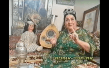 Zohra El Fassia speaking in a Haim Shiran film, instrument, doll, and art in the background