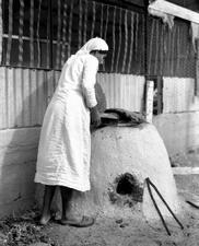 A Yemenite Jewish woman next to the traditional baking oven at Moshav Elyashiv, 1939