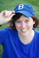 Jessie Atkin wearing blue t-shirt and blue baseball cap posing in front of grass