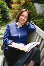 Claudia Roden sitting on a bench in a garden, with an open book in her lap