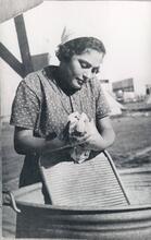 A woman washes laundry by hand with a tin tub and washboard.
