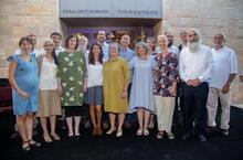 A group of ten men and seven women, smiling and standing in front of a building labeled "Segal Beit Midrash" in English and Hebrew