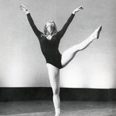 Cecilia Baram dancing, one leg lifted above her waist, both arms raised and her face tilted up