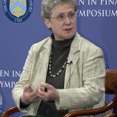 Abby Joseph Cohen speaking while seated in a chair in front of a symposium backdrop