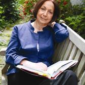 Claudia Roden sitting on a bench in a garden, with an open book in her lap