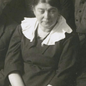 A group photo cropped to show just Esther Frumkin, wearing a plain black dress with an attached white collar