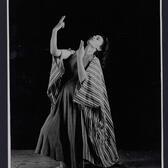 Paula Padani, in black and white, dancing with her arms in the air. 