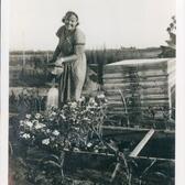 A smiling woman stands behind a planter box watering flowers