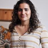 Erez Zobary is smiling at the camera, she has curly brown hair and is wearing a striped top.