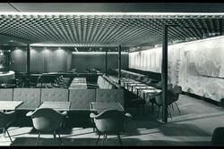 A room with a low, textured ceiling, full of tables, chairs, and booths