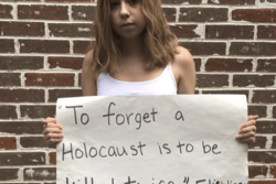 High school student standing in front of a brick wall. She is holding a protest sign that says "To forget a Holocaust is to be killed twice," attributed to Elie Wiesel.