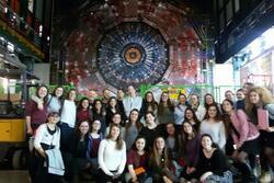 A large group of high school girls and some adults posing in front of the Large Hadron Collider