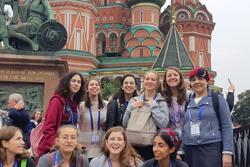 A group of high school girls and a chaperone pose in front of St. Basil's Cathedral