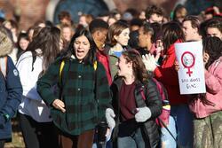Shoshannah Hemley and another student stand in front of a crowd of students, shouting in protest. Someone in the crowd holds a sign that says "girls against guns." 