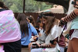Young woman wearing tefillin and holding a prayer book during a service. Surrounded by fellow campers.